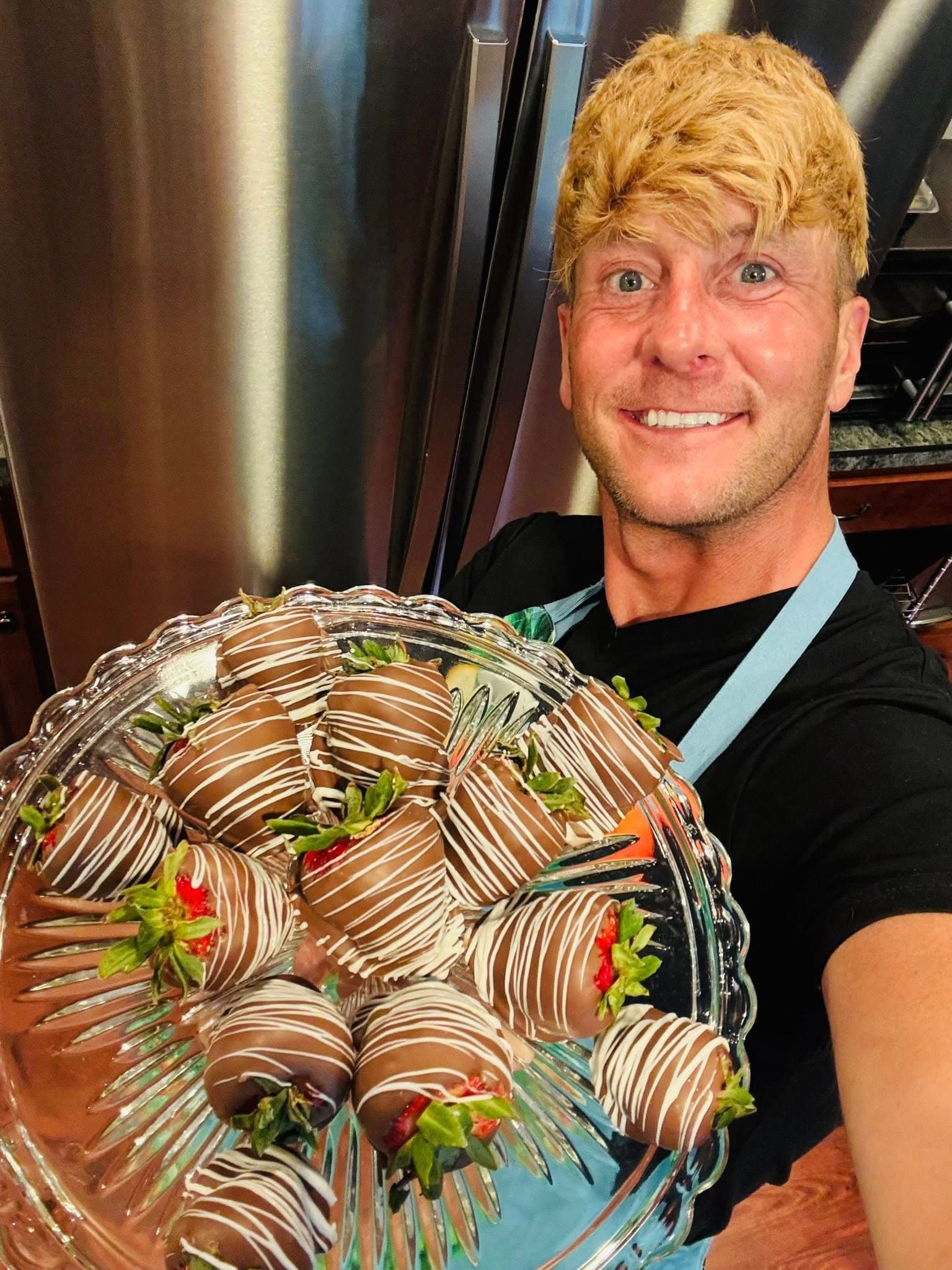 A person smiles while holding a platter of chocolate-covered strawberries.