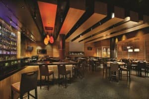 A modern restaurant interior featuring a bar, wooden accents, and ambient lighting.