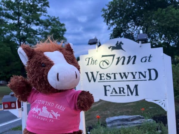 A plush horse wearing a pink shirt stands in front of the sign for The Inn at Westwynd Farm.