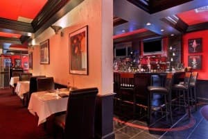 Interior of an upscale restaurant featuring red walls, black seating, and a bar area.