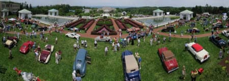 A panoramic view of a car show with vintage vehicles and attendees in a lush garden setting.