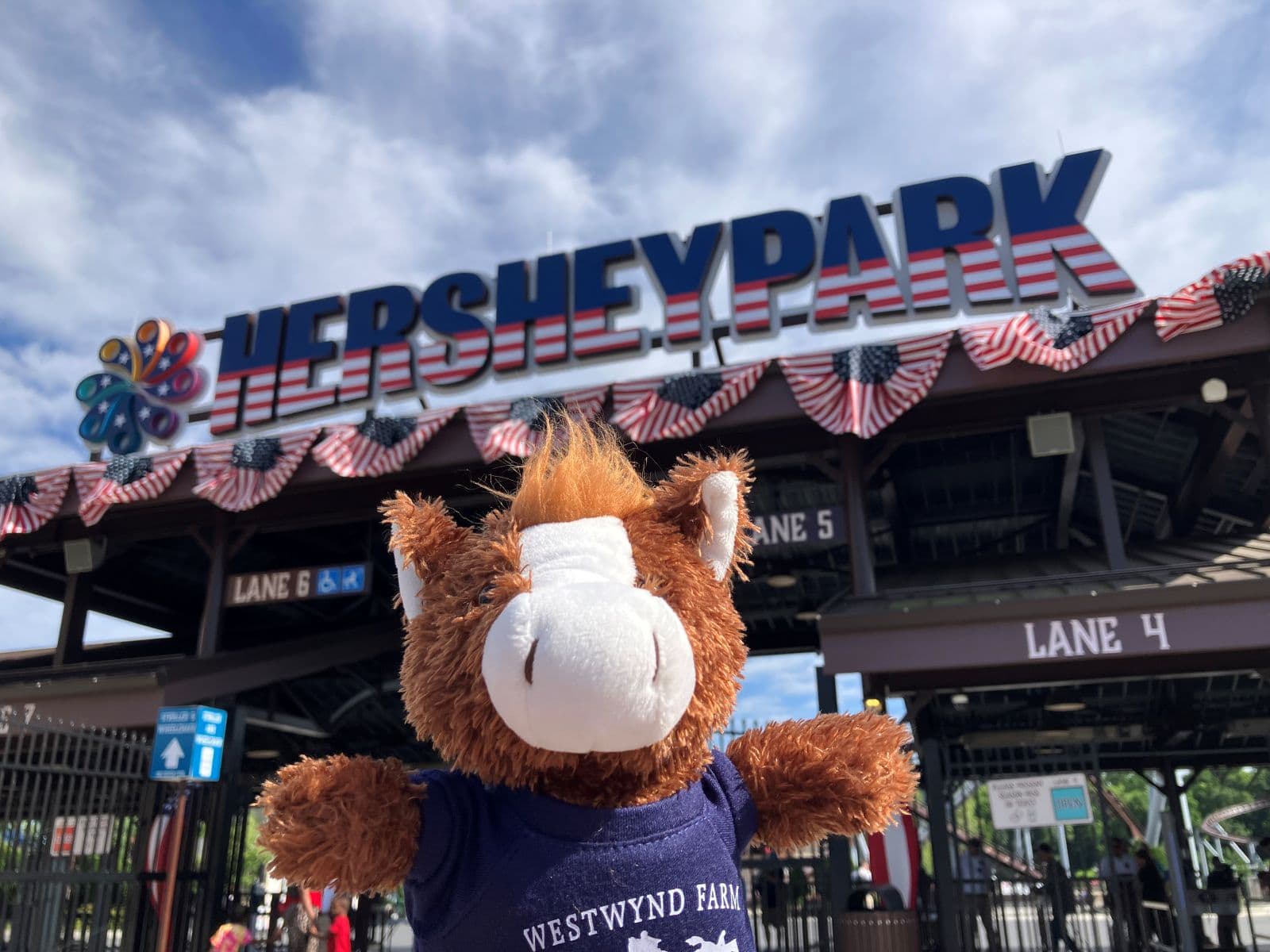 A plush horse toy stands in front of the Hersheypark entrance sign.