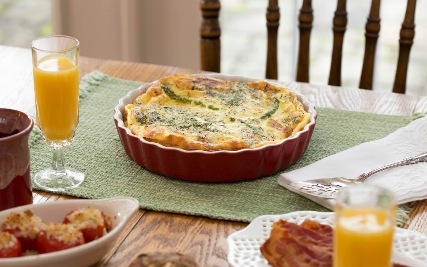 A table setting featuring a baked dish, a glass of orange juice, and various side dishes. A table setting featuring a baked dish, a glass of orange juice, and various side dishes.