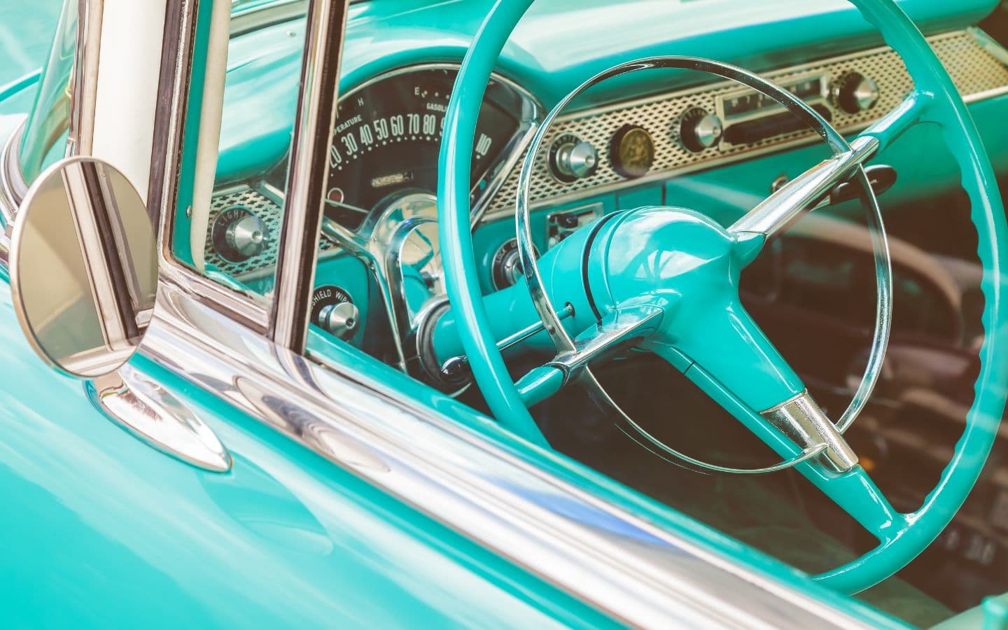 A vintage car interior featuring a turquoise steering wheel and dashboard.