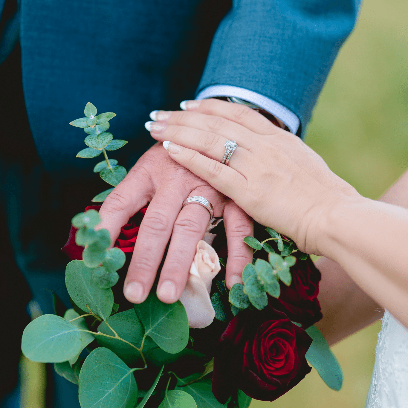 A close-up of two hands adorned with wedding rings, resting on a bouquet of roses and greenery.