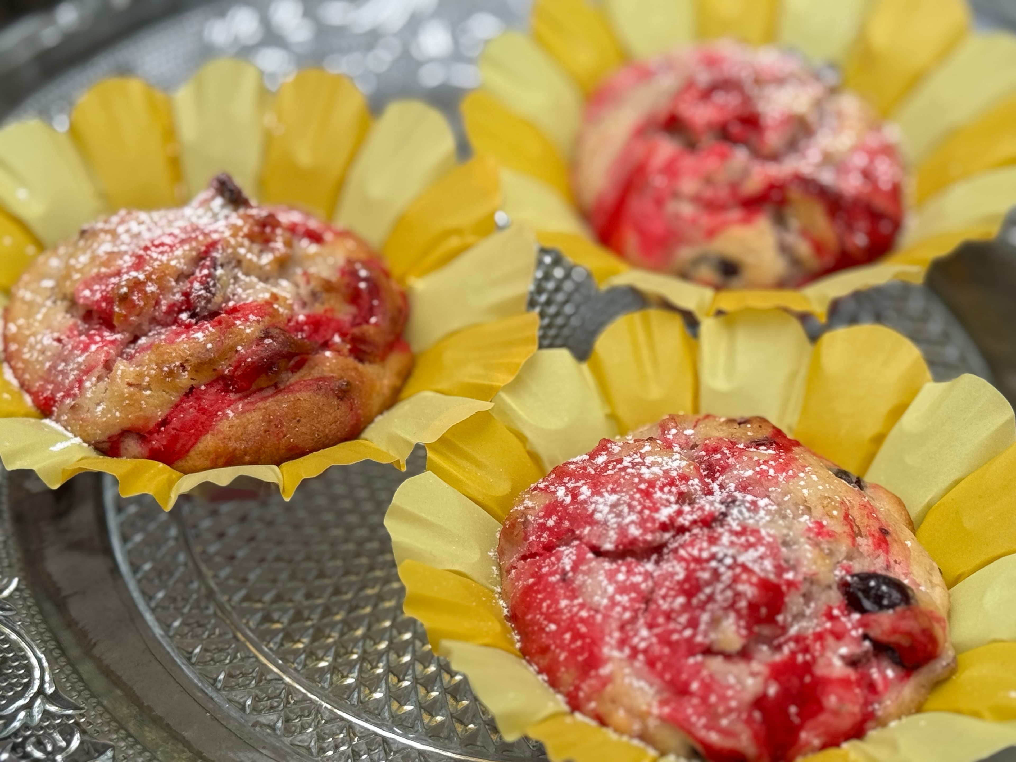Three colorful pastries in yellow cups, dusted with powdered sugar.