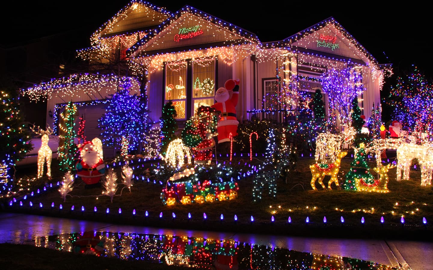 A house decorated with colorful Christmas lights and festive decorations, including Santa and reindeer.