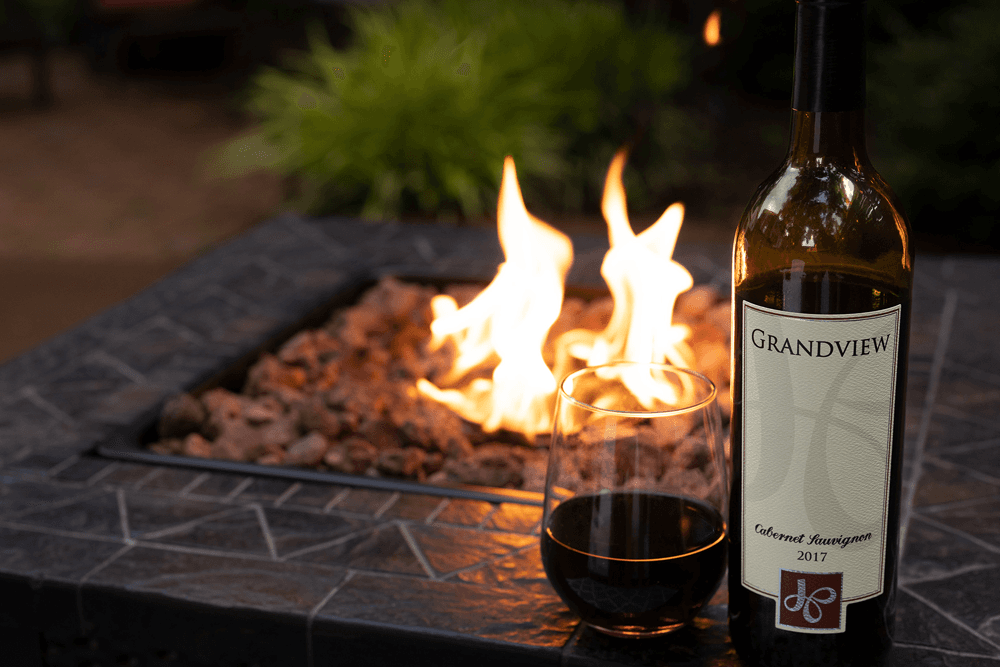 A bottle of Grandview Cabernet Sauvignon next to a glass of red wine, with a fire pit ablaze in the background.