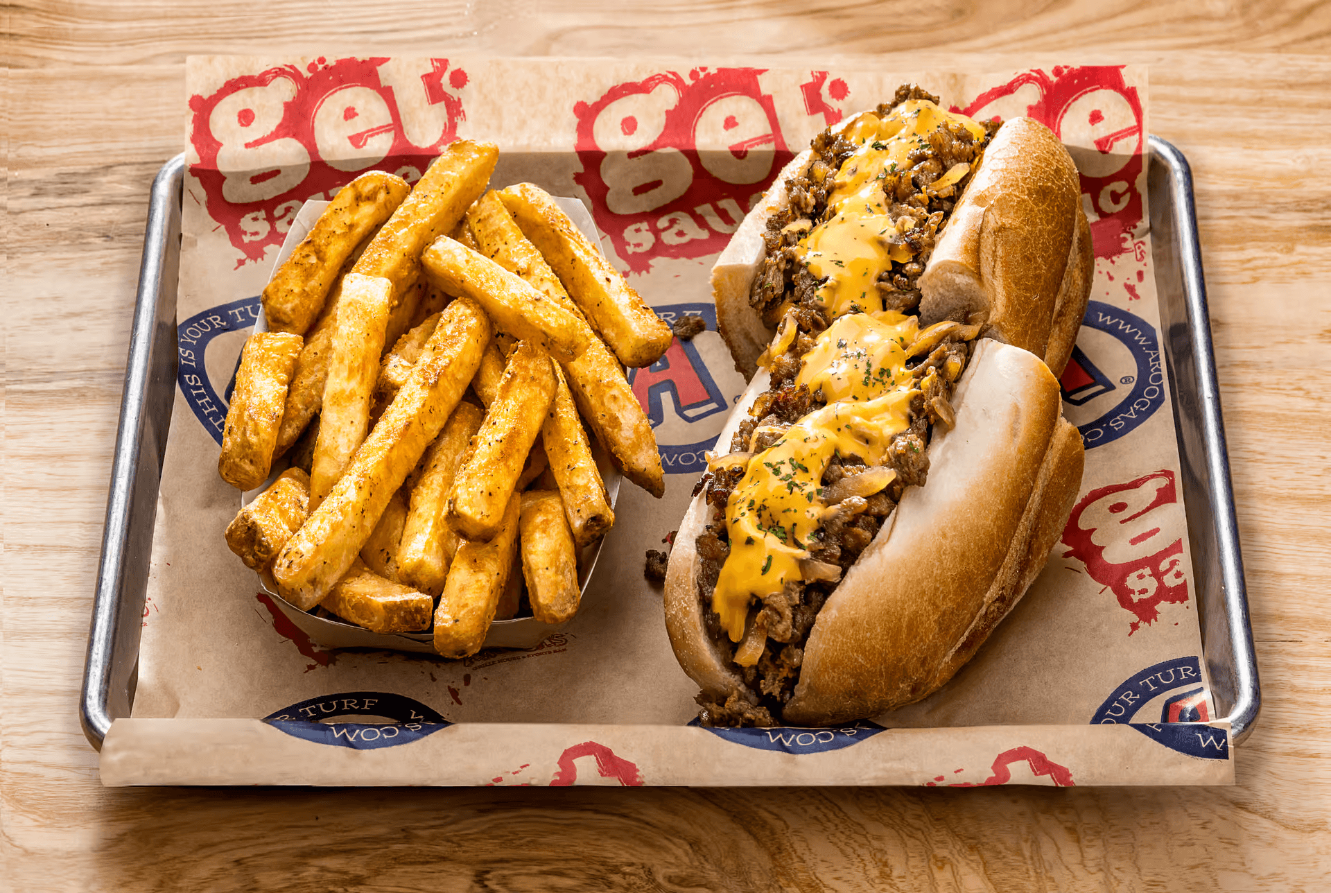 A tray with a loaded cheese steak sandwich and golden, crispy fries on parchment paper.