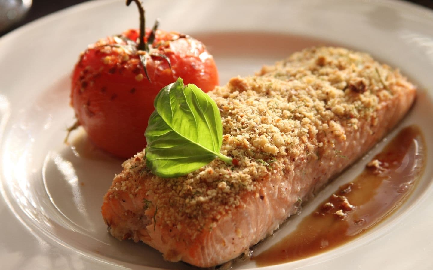 A plated dish featuring baked salmon with a crispy topping, garnished with a basil leaf and accompanied by a roasted tomato. A plated dish featuring baked salmon with a crispy topping, garnished with a basil leaf and accompanied by a roasted tomato.
