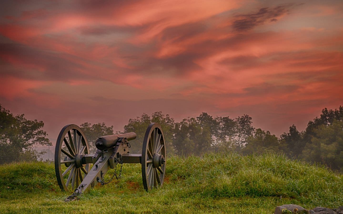 An antique cannon rests on a grassy hillside under a vibrant sunset sky. An antique cannon rests on a grassy hillside under a vibrant sunset sky.