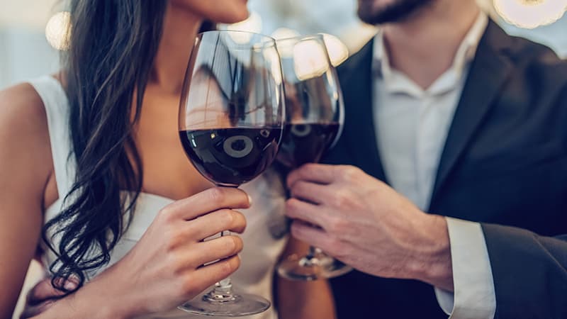A couple clinks wine glasses together, celebrating in a romantic setting.