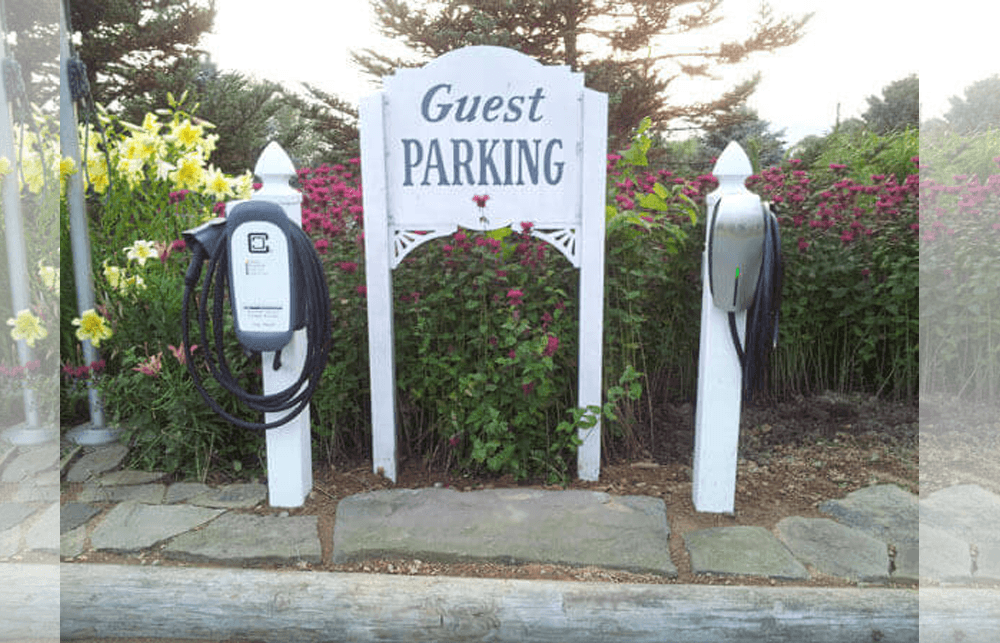 Sign for guest parking with two electric vehicle charging stations surrounded by colorful flowers.