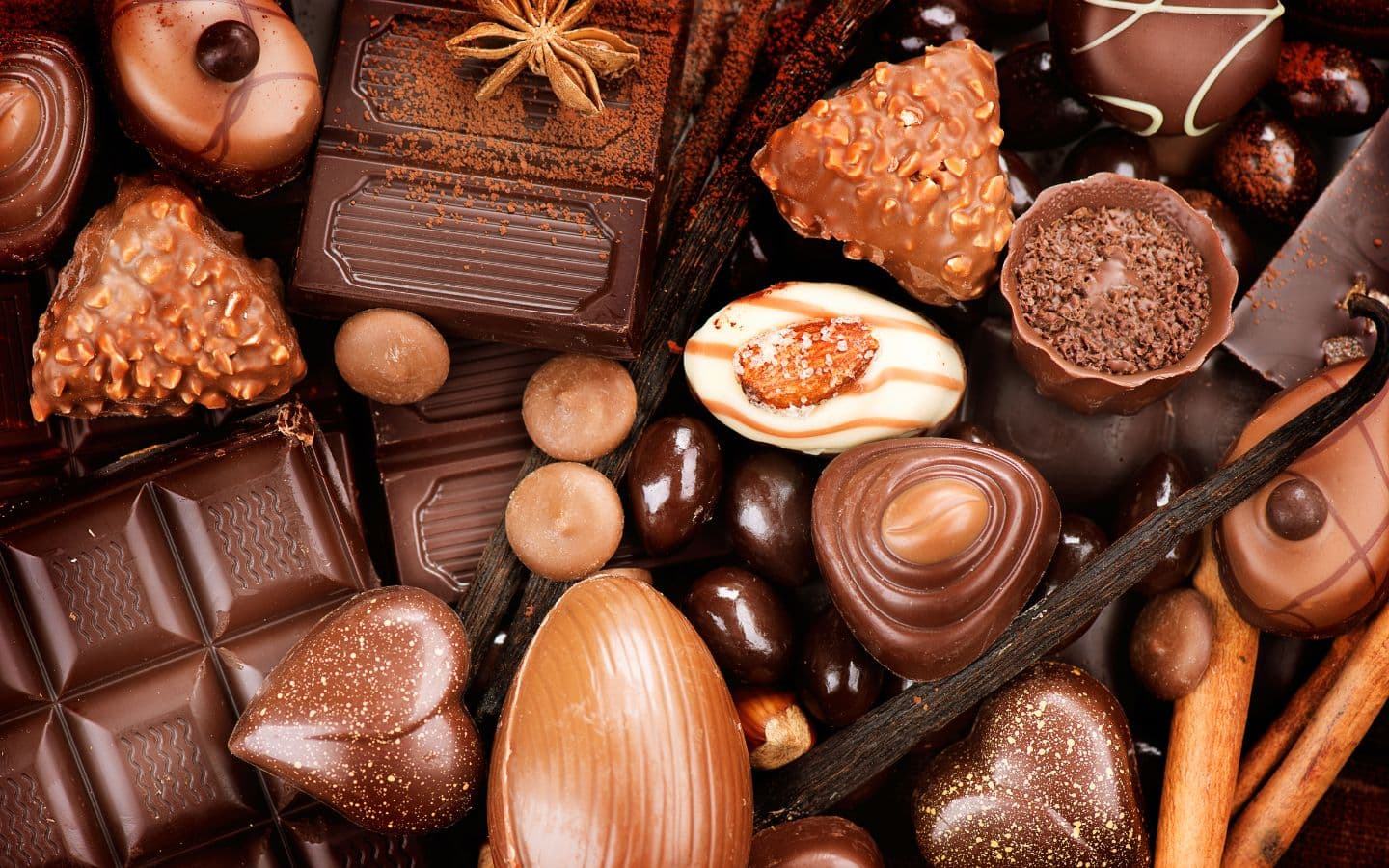 A variety of gourmet chocolates, including bars, truffles, and shaped confections, arranged enticingly on a wooden surface.