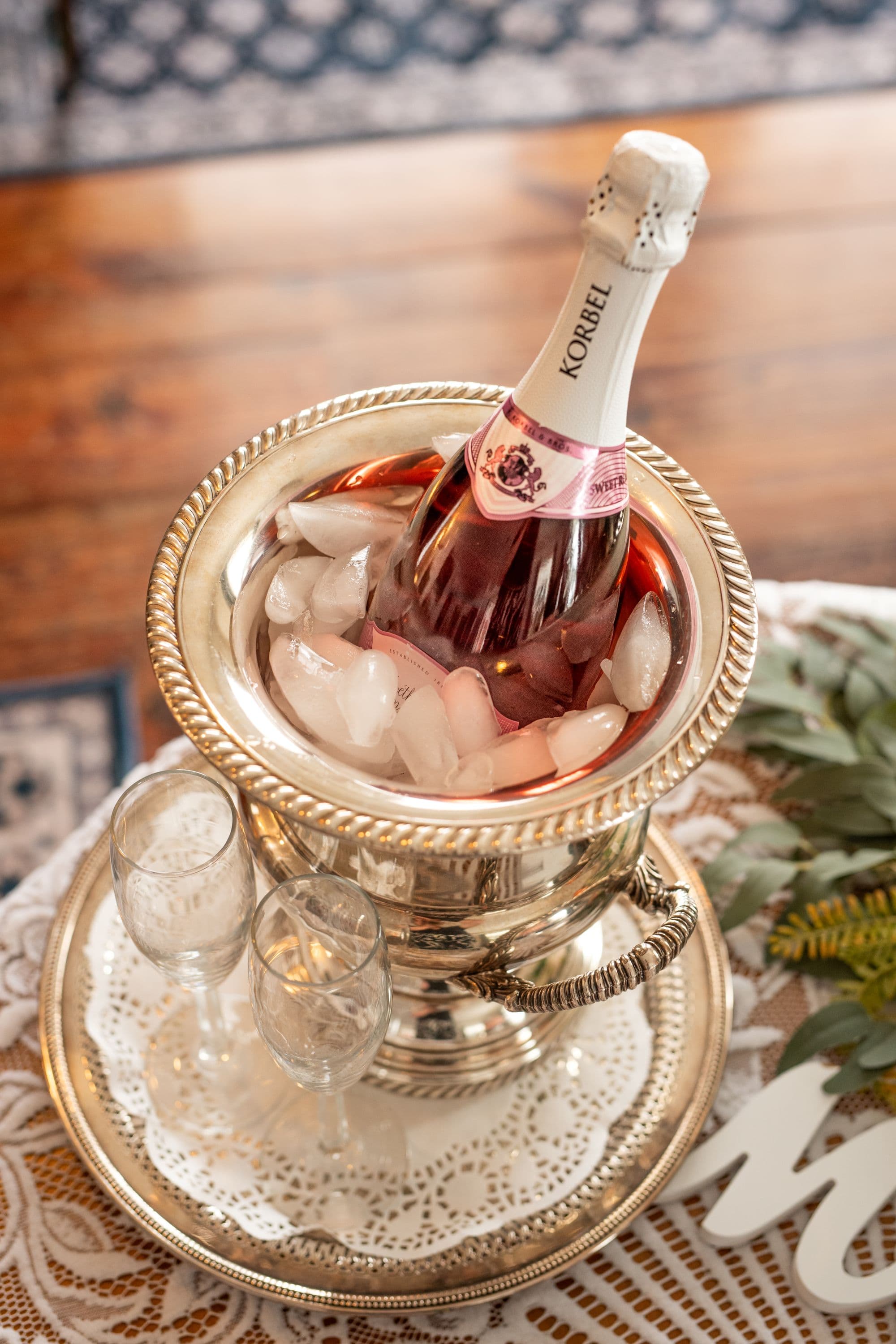 A bottle of Korbel champagne is chilled in a silver ice bucket surrounded by ice, with two empty champagne flutes beside it.