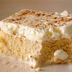 A slice of moist cake topped with whipped cream and a sprinkle of cinnamon.