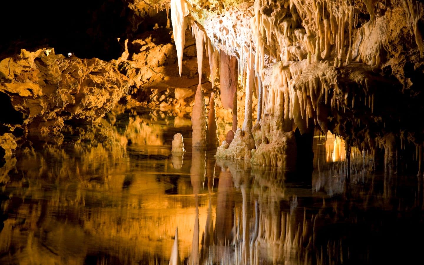 A serene underground cave with stalactites reflected in still water illuminated by soft golden light.