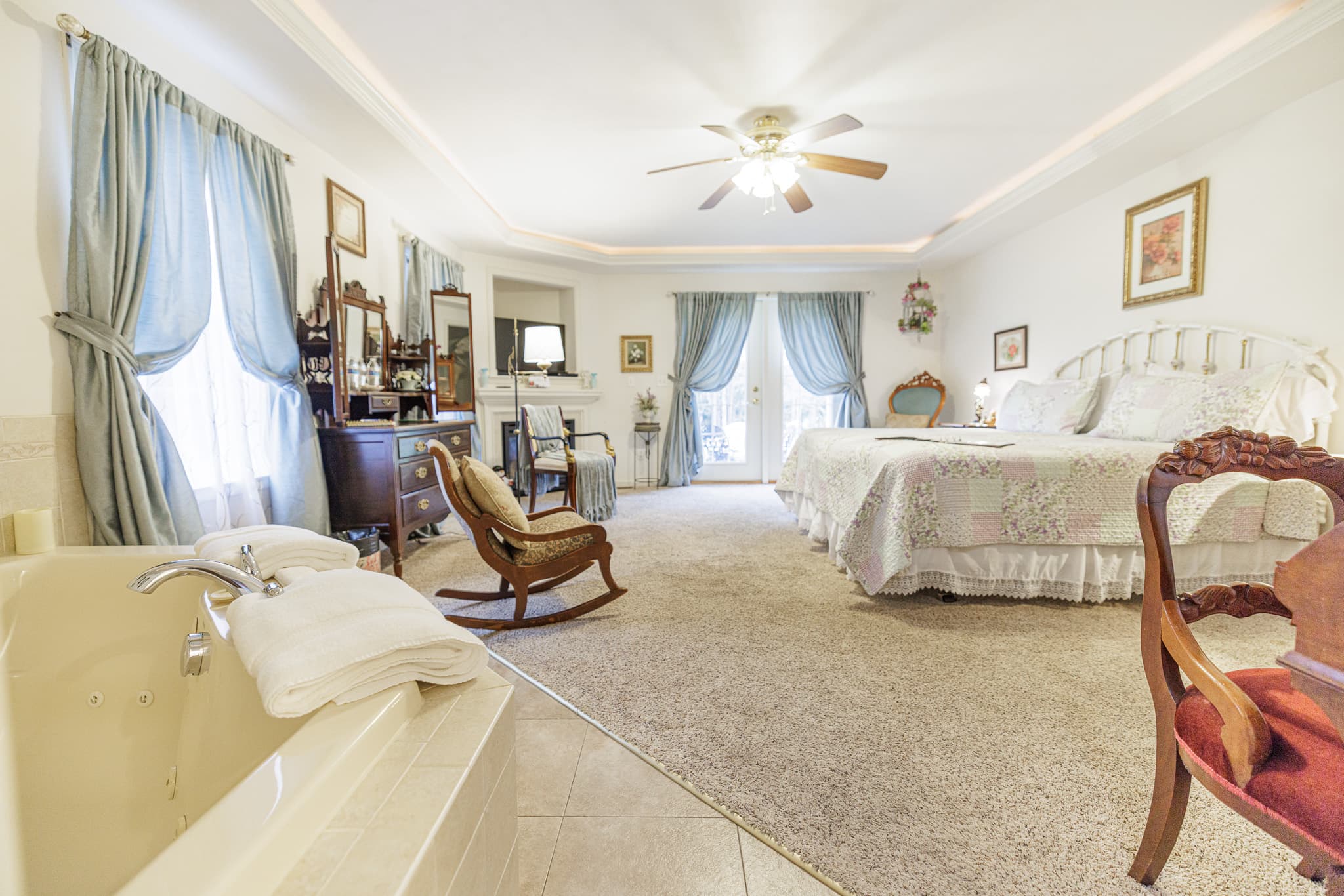 A spacious, well-decorated bedroom featuring a large bed, armchair, and a spa-like tub.