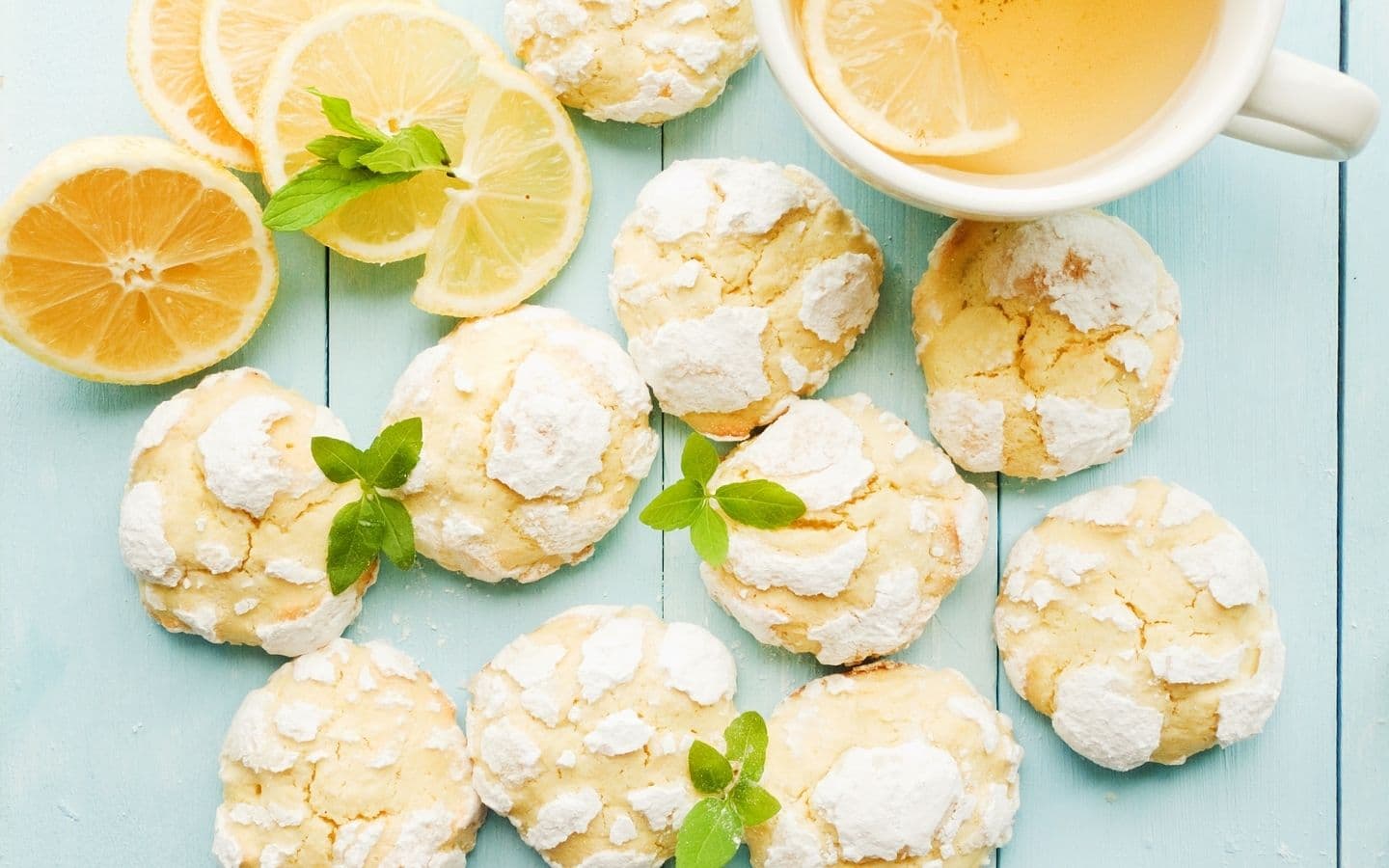 A plate of lemon cookies garnished with mint, alongside lemon slices and a cup of tea. A plate of lemon cookies garnished with mint, alongside lemon slices and a cup of tea.