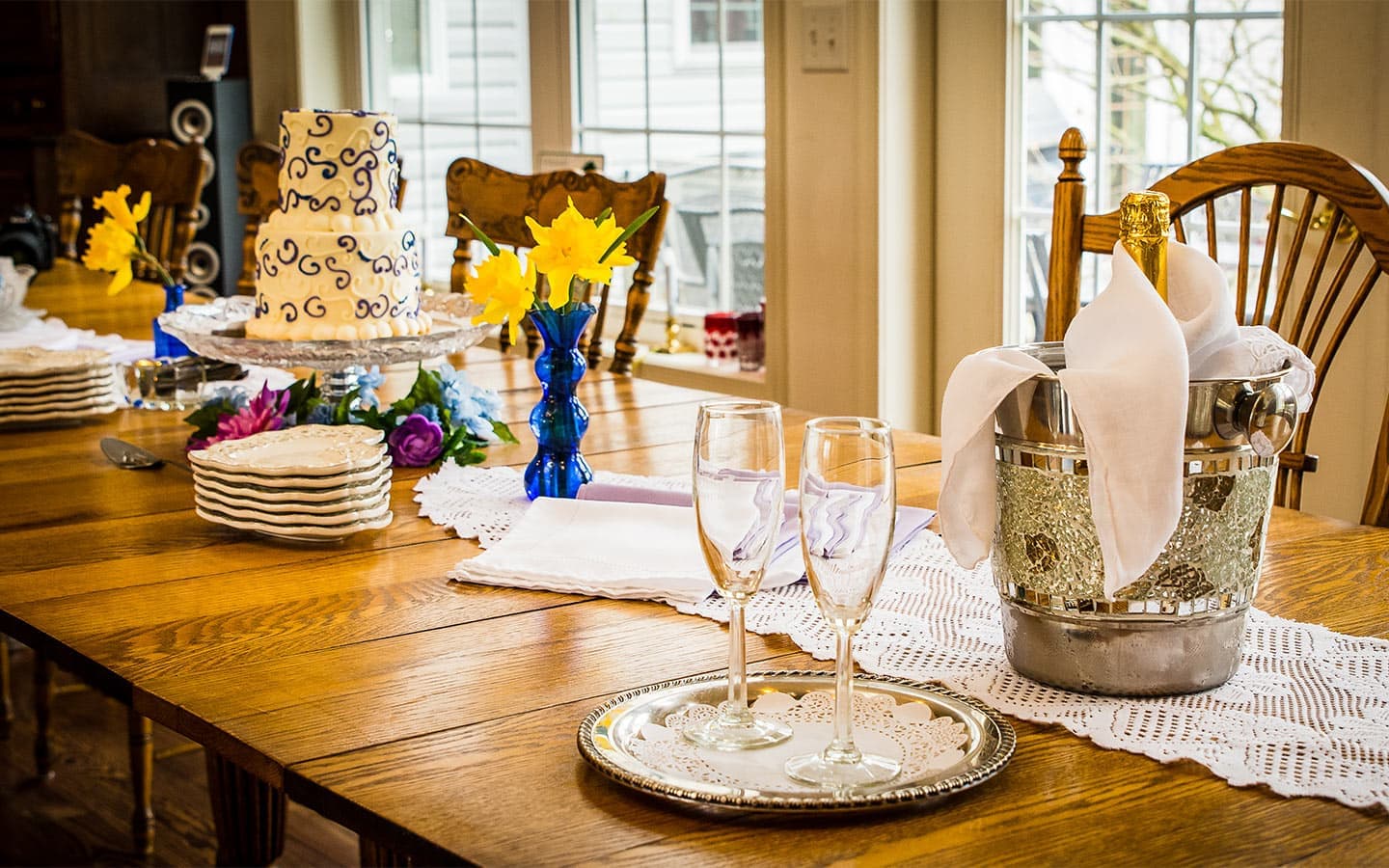 A beautifully set dining table featuring a two-tiered cake, floral arrangements, champagne, and elegant glassware.