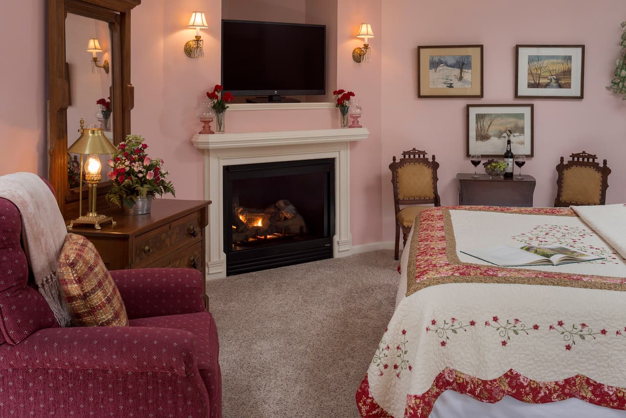 pink walls, comfy chair near fireplace at foot of bed