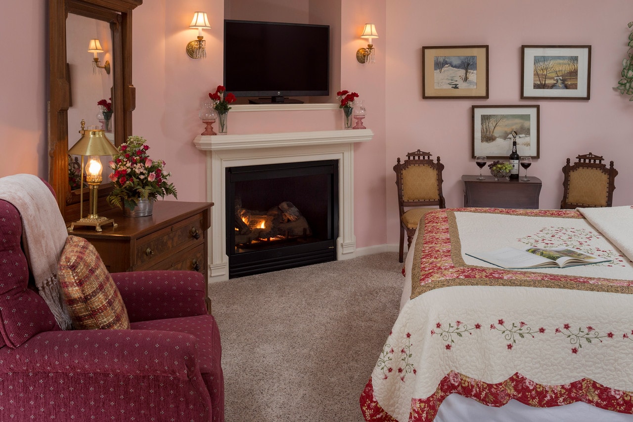 pink walls, comfy chair near fireplace at foot of bed