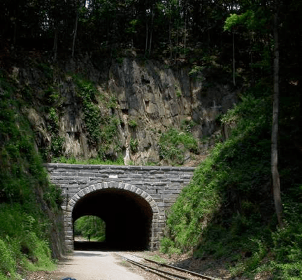 A stone archway tunnel under a rocky hillside with greenery on either side.
