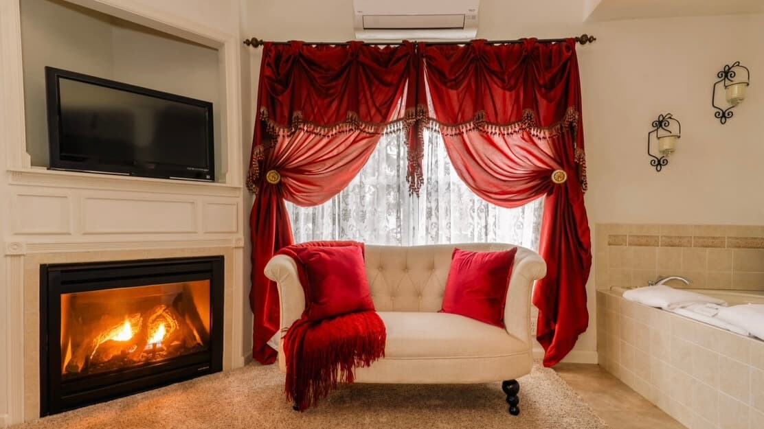Cozy sitting area with a cream sofa, red pillows, and dramatic red curtains beside a fireplace. Cozy sitting area with a cream sofa, red pillows, and dramatic red curtains beside a fireplace.