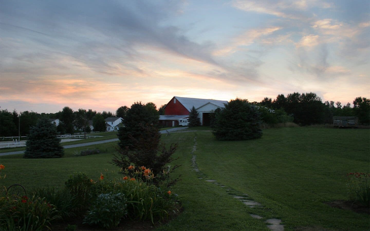 A serene countryside scene featuring a barn at sunset, surrounded by greenery and flowers.