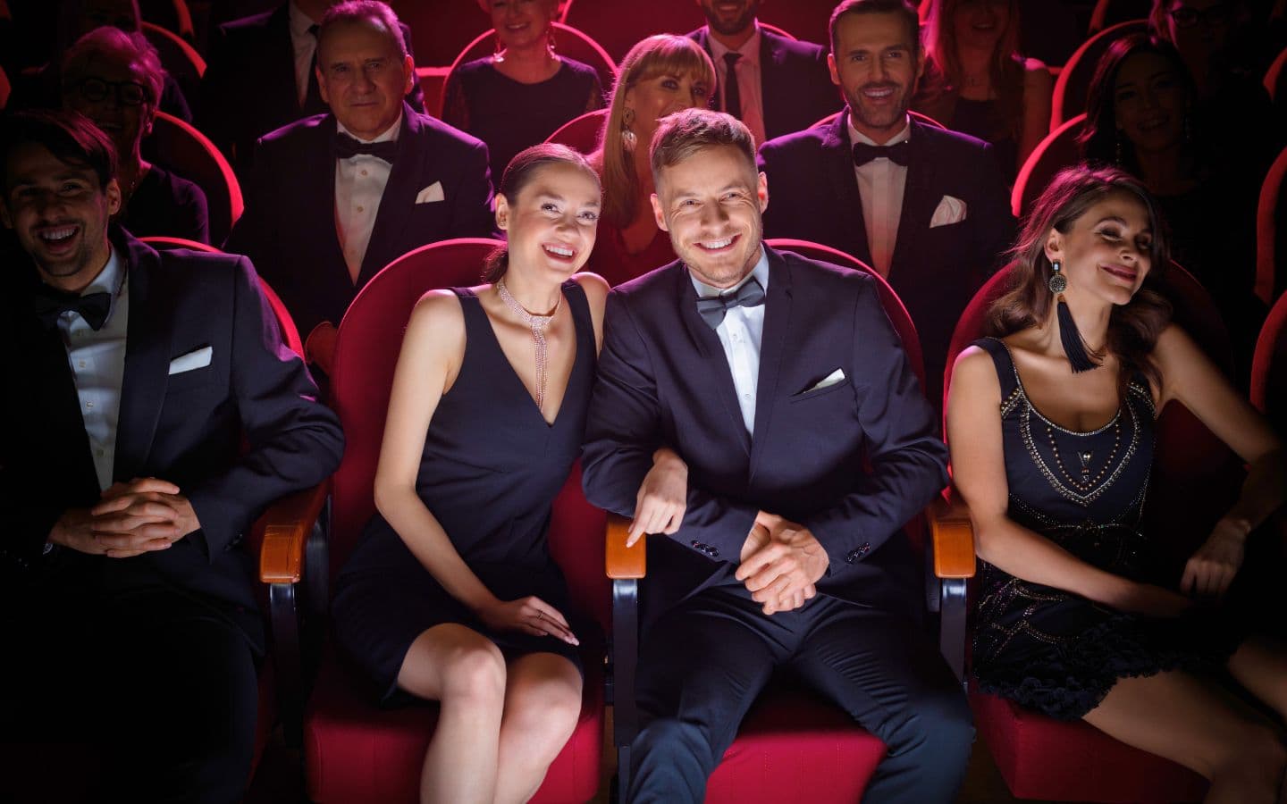 A group of elegantly dressed people smiles and poses in a theater seating.