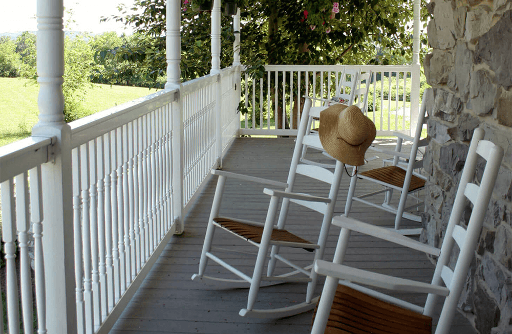 A porch with white rocking chairs and a straw hat resting on the railing.