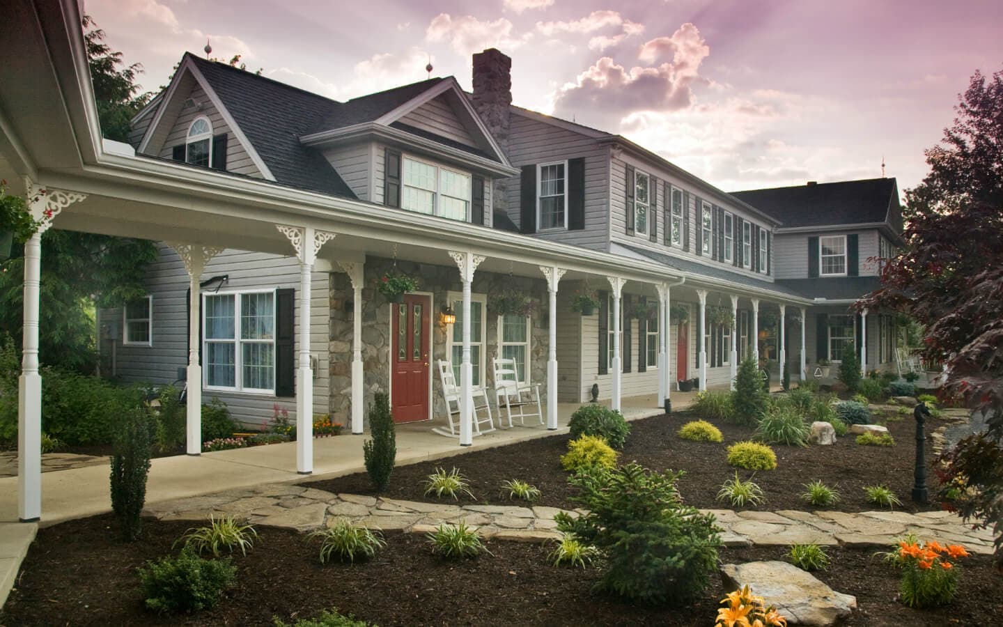 A charming gray house with a porch, surrounded by lush landscaping and colorful flowers.