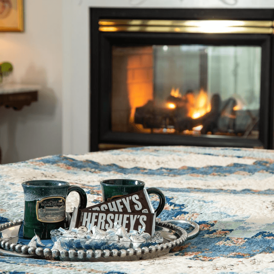 Two green mugs and Hershey's chocolate on a tray in front of a cozy fireplace.