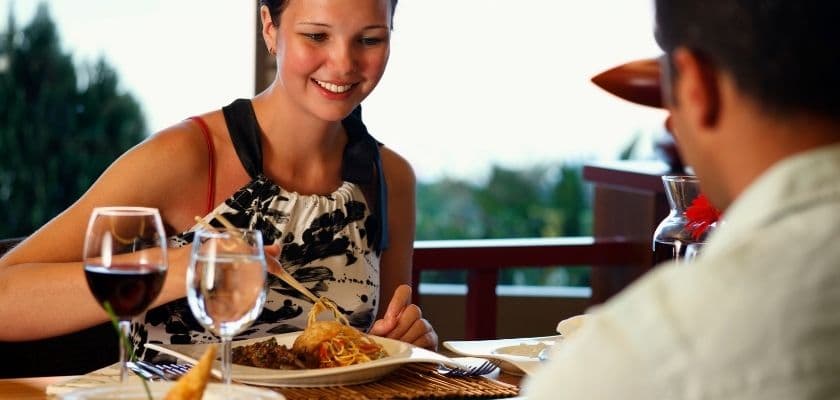 A woman smiles while enjoying a meal at a restaurant with a man out of focus.