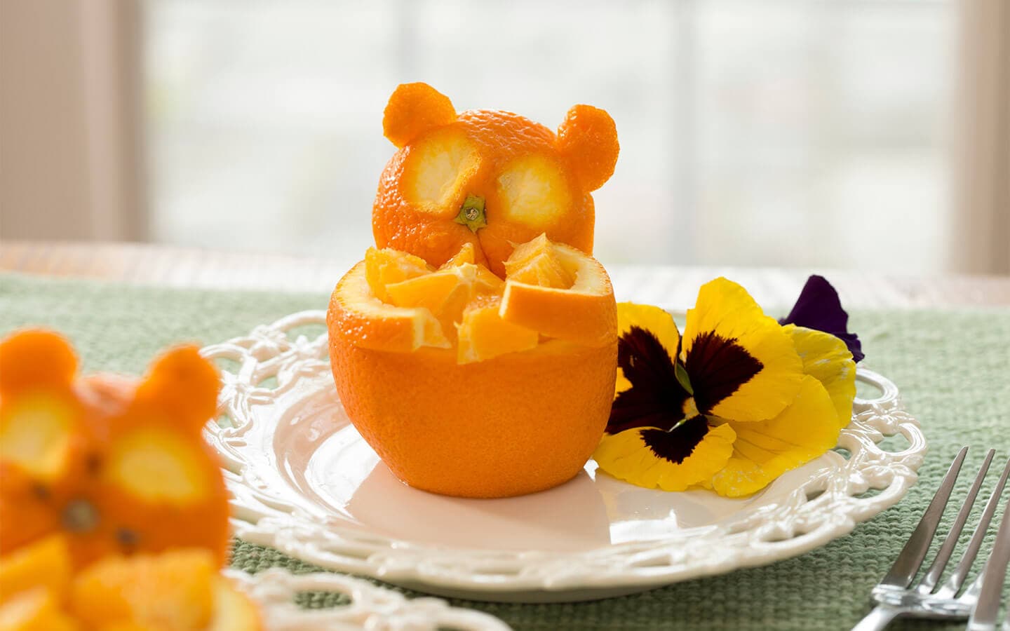 A creatively carved orange resembling a bear sits atop a plate with colorful flower petals.