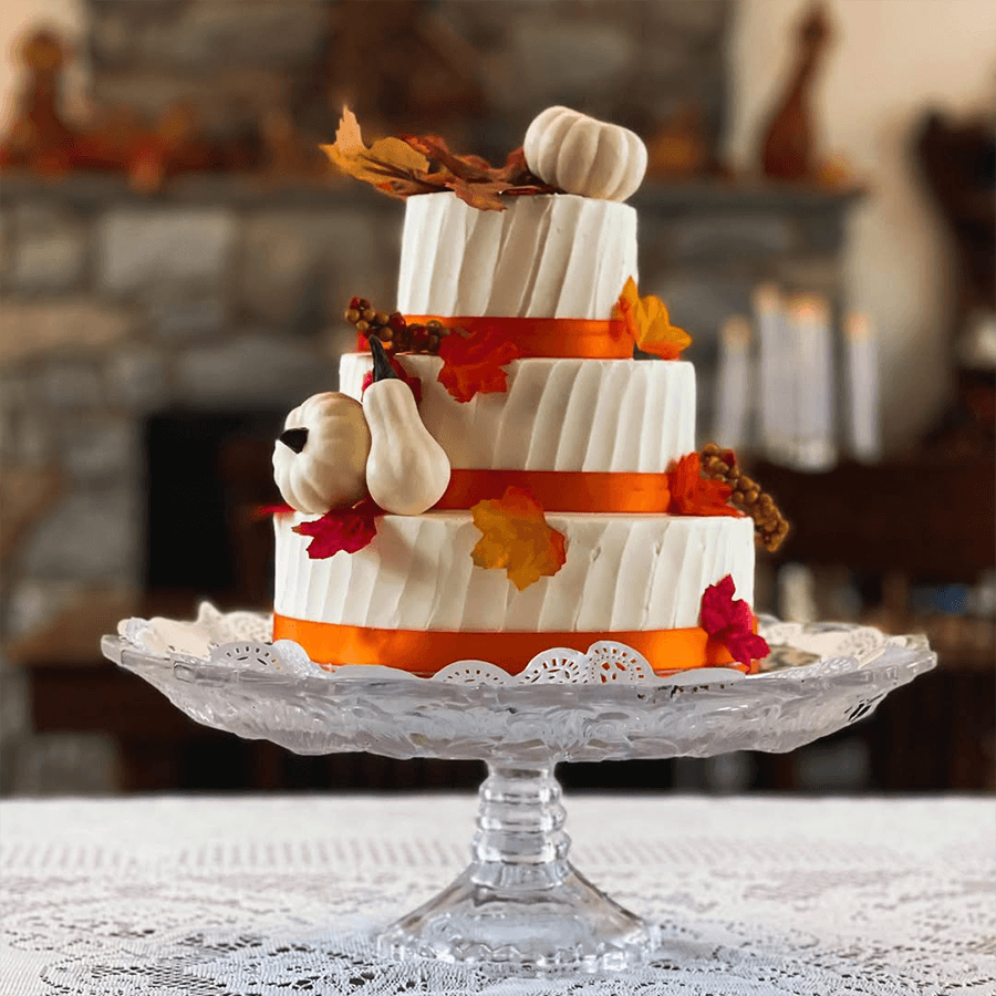 A three-tiered white cake decorated with autumn leaves and small white pumpkins.