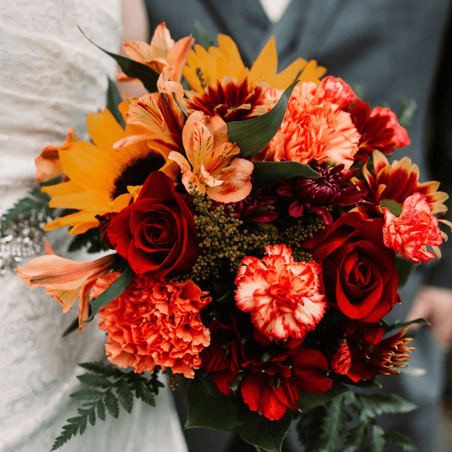 A vibrant bouquet featuring red roses, orange lilies, sunflowers, and assorted colorful blooms.