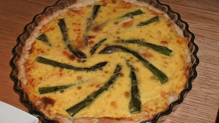 A savory pie featuring a spiral arrangement of asparagus on a creamy filling.