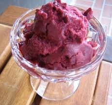 A bowl of deep purple sorbet rests on a wooden surface.