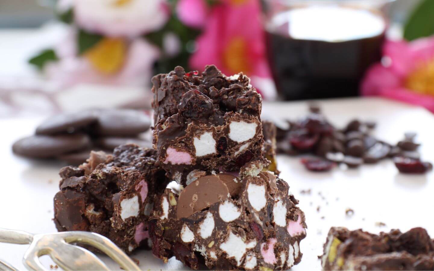 Chocolate marshmallow squares with pink and white pieces, surrounded by flowers and chocolate ingredients. Chocolate marshmallow squares with pink and white pieces, surrounded by flowers and chocolate ingredients.