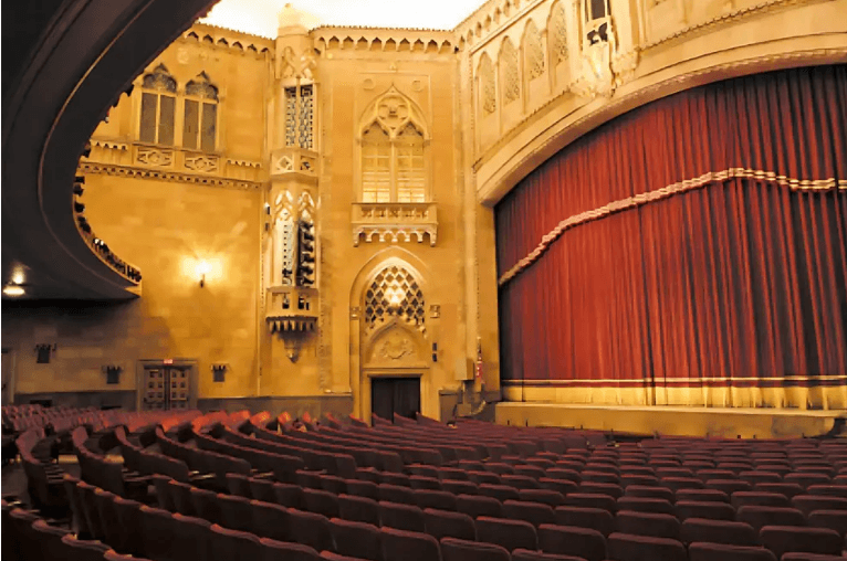 An ornate theater interior featuring red velvet curtains and plush seating.