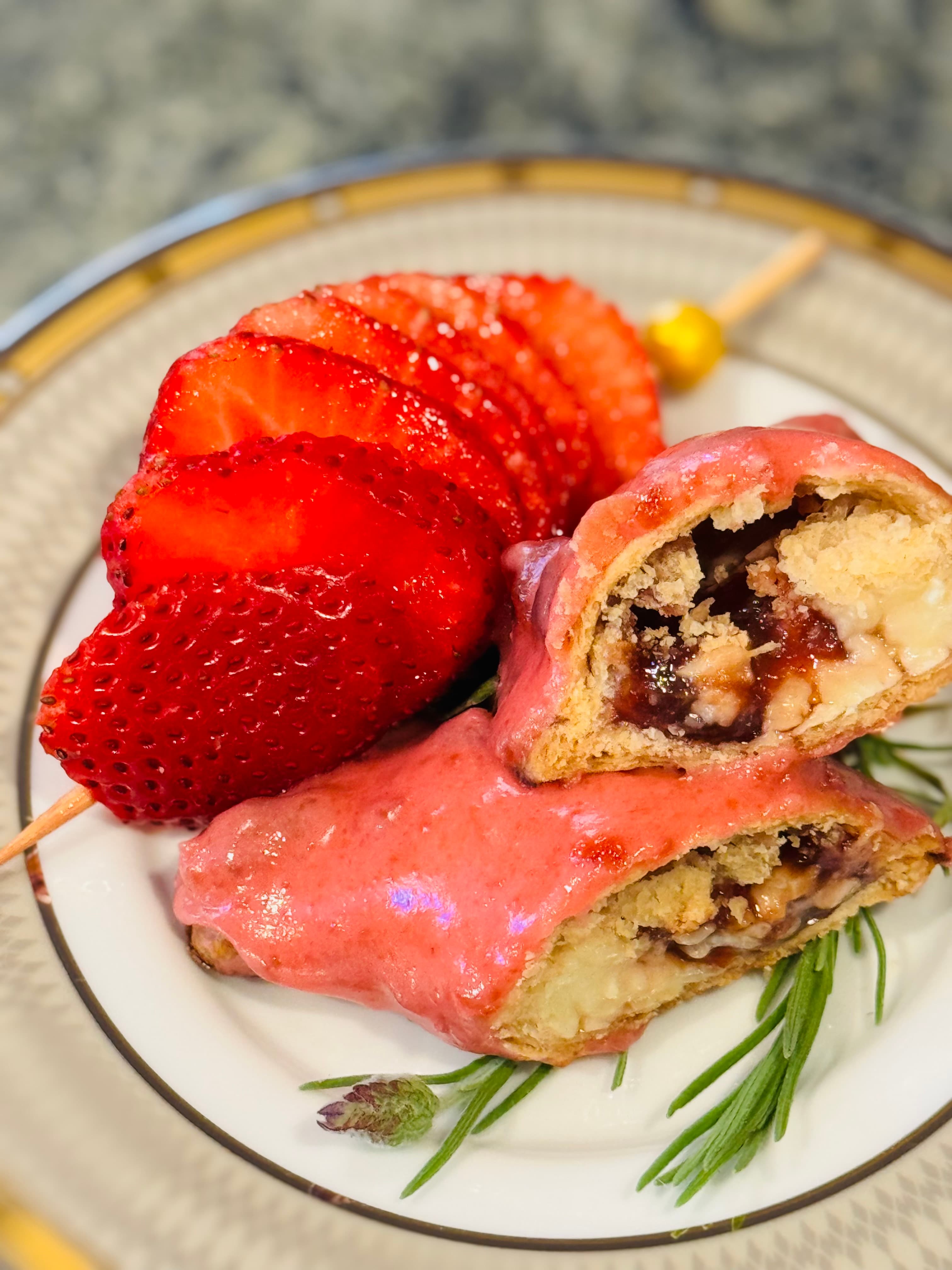 A plate featuring sliced strawberries and a sweet pastry filled with fruit, topped with pink icing.