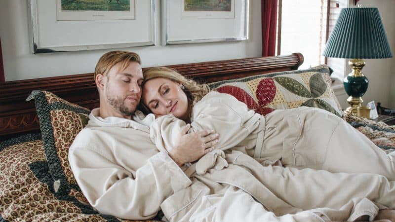 A couple relaxes together in matching robes on a cozy bed.