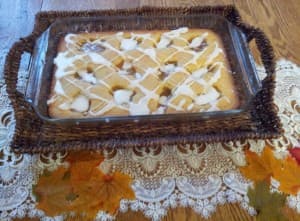 A baked dessert drizzled with icing, served in a glass dish on a decorative tablecloth.