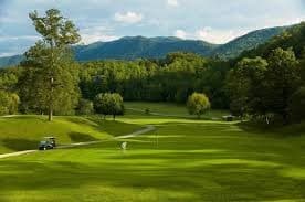 A scenic golf course with rolling green hills and distant mountains under a partly cloudy sky.