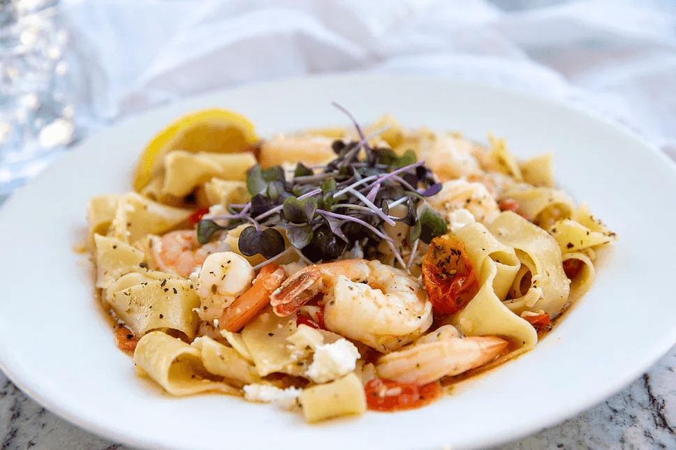 A plate of pasta with shrimp, herbs, and microgreens, garnished with a lemon wedge.