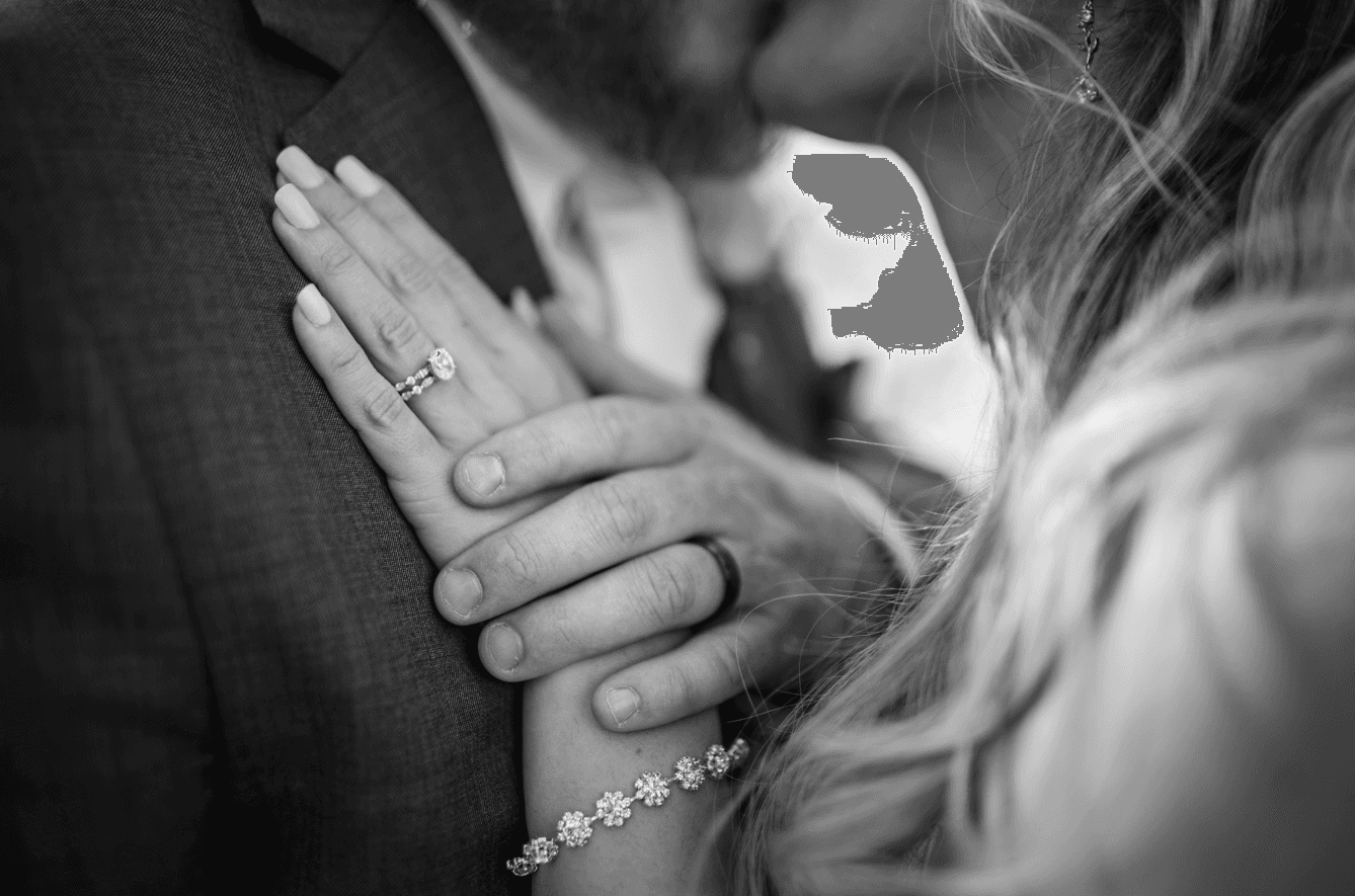 Close-up of entwined hands featuring wedding rings, with a couple in a romantic embrace.