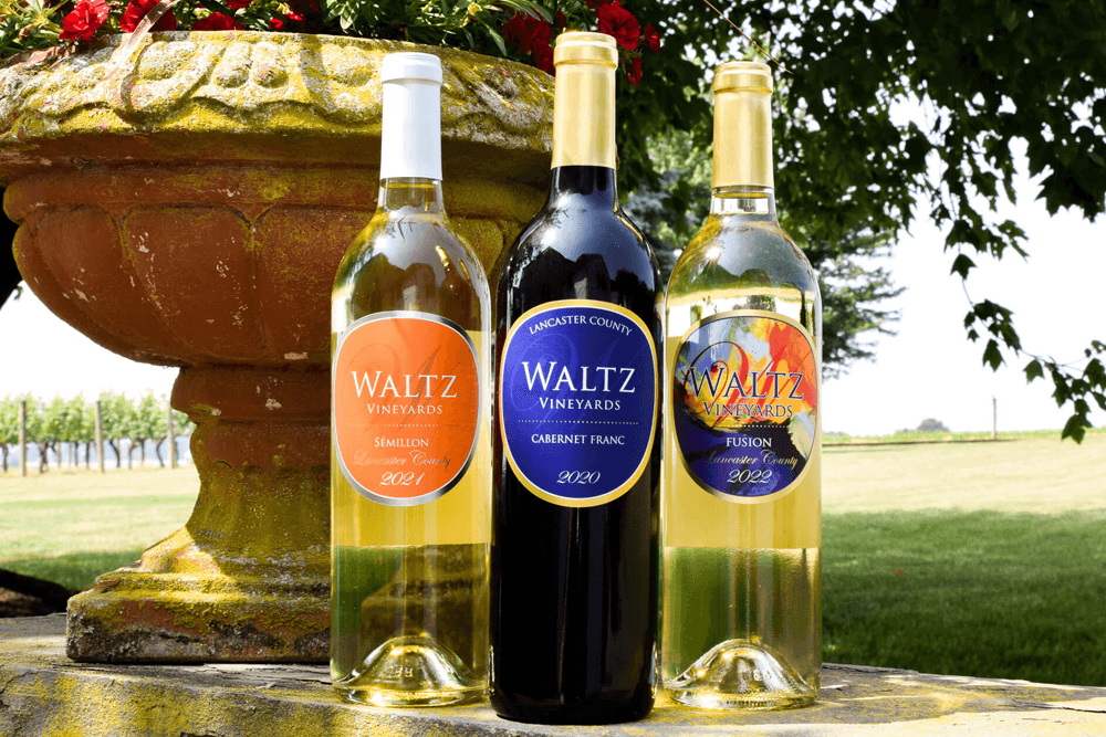 Three bottles of Waltz Vineyards wine, including Sémitillon, Cabernet Franc, and Fusion, displayed outdoors near a flower pot.