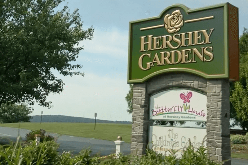 Sign for Hershey Gardens featuring "Butterfly House" and "The Children's Garden" with greenery in the background.