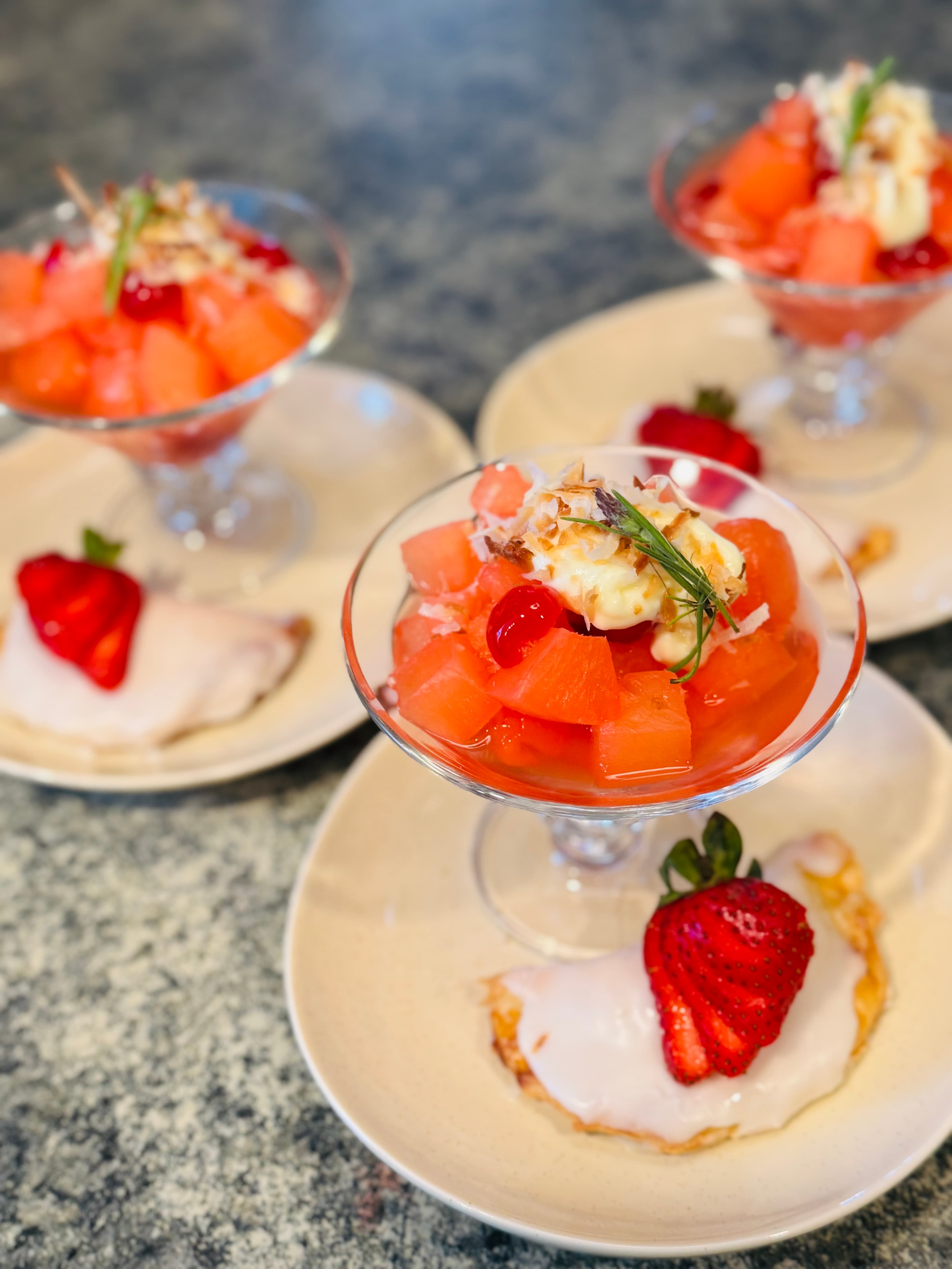 A colorful dessert spread featuring fruit cups with melon and cherries, accompanied by a sweet pastry topped with strawberry.